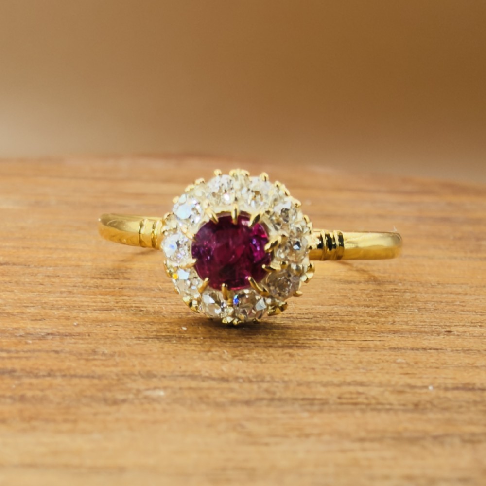 An 18ct yellow gold Victorian ring featuring a central round red ruby surrounded by a halo of hand-cut diamonds. View VI