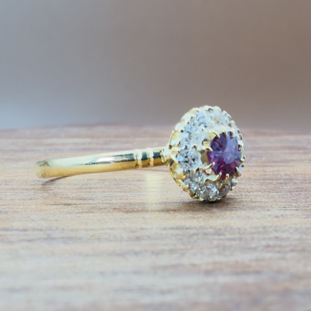 An 18ct yellow gold Victorian ring featuring a central round red ruby surrounded by a halo of hand-cut diamonds. View VII