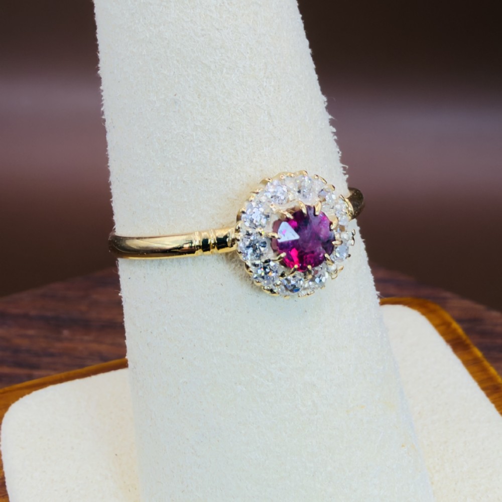 An 18ct yellow gold Victorian ring featuring a central round red ruby surrounded by a halo of hand-cut diamonds. View X