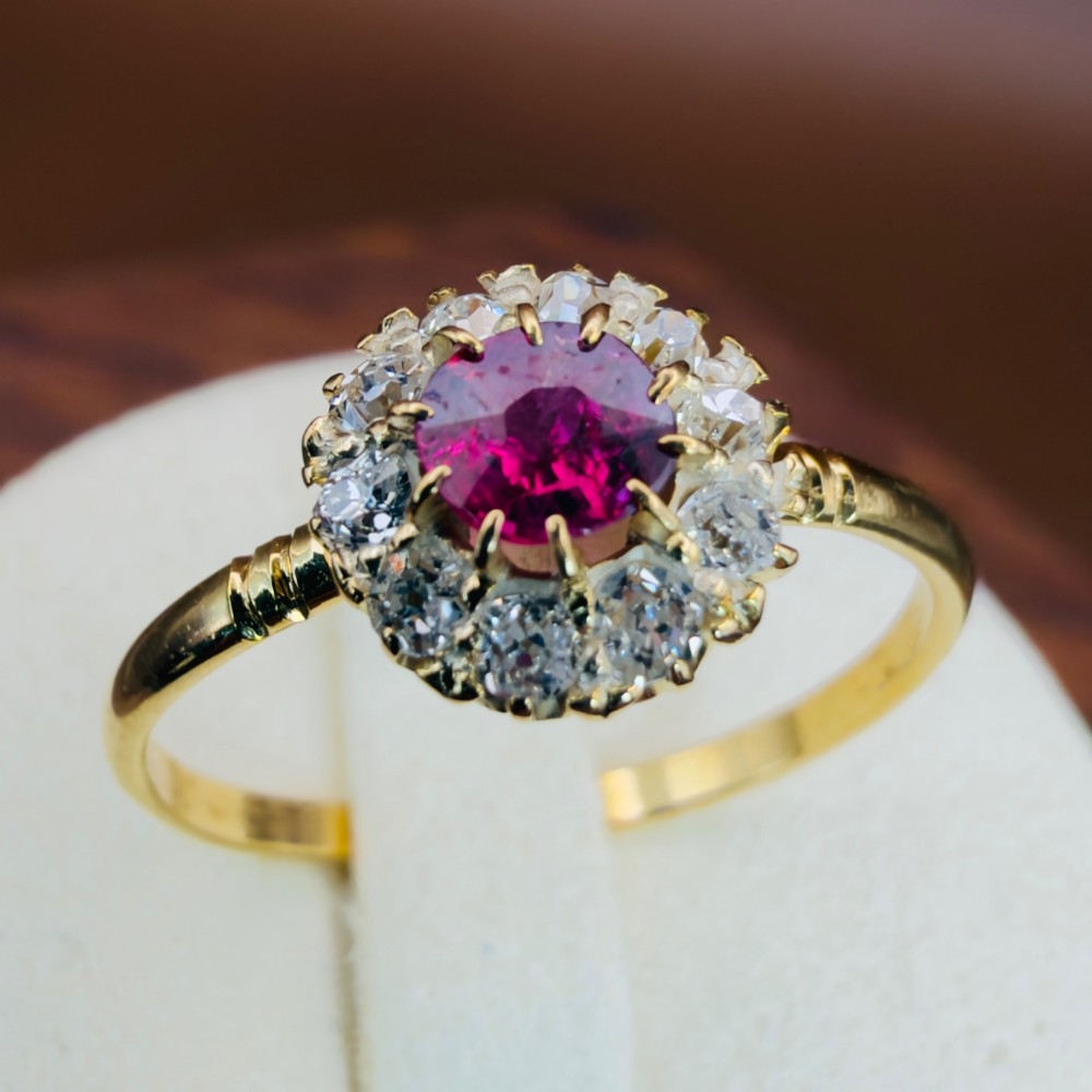 An 18ct yellow gold Victorian ring featuring a central round red ruby surrounded by a halo of hand-cut diamonds.