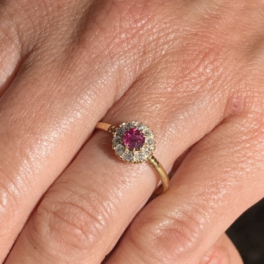 An 18ct yellow gold Victorian ring featuring a central round red ruby surrounded by a halo of hand-cut diamonds. View XV