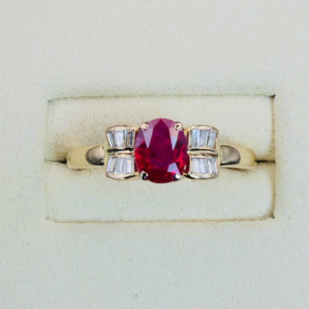 An 18ct yellow gold ring featuring an oval cut central red ruby flanked by stepped baguette cut diamonds on a polished band. View II