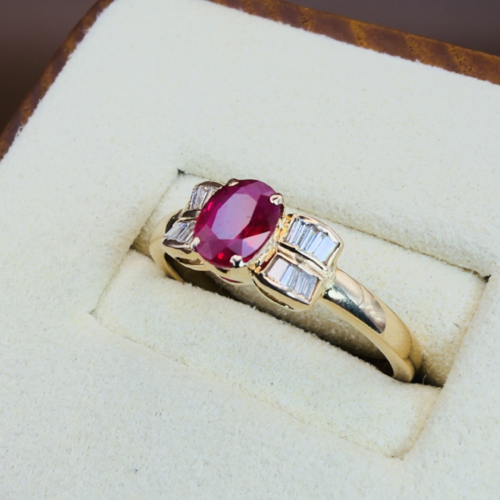 An 18ct yellow gold ring featuring an oval cut central red ruby flanked by stepped baguette cut diamonds on a polished band. View III