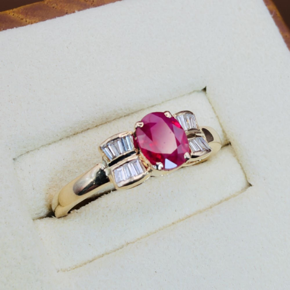 An 18ct yellow gold ring featuring an oval cut central red ruby flanked by stepped baguette cut diamonds on a polished band. View IV