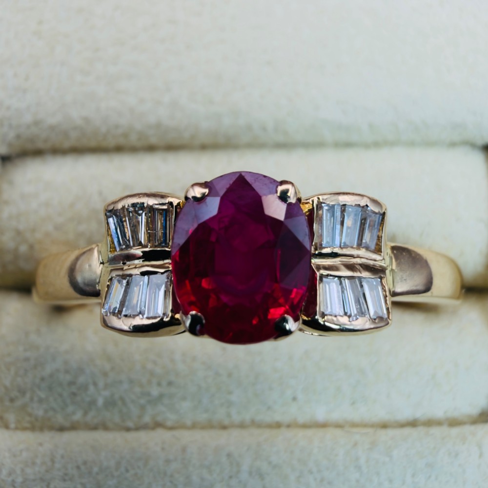 An 18ct yellow gold ring featuring an oval cut central red ruby flanked by stepped baguette cut diamonds on a polished band. View V