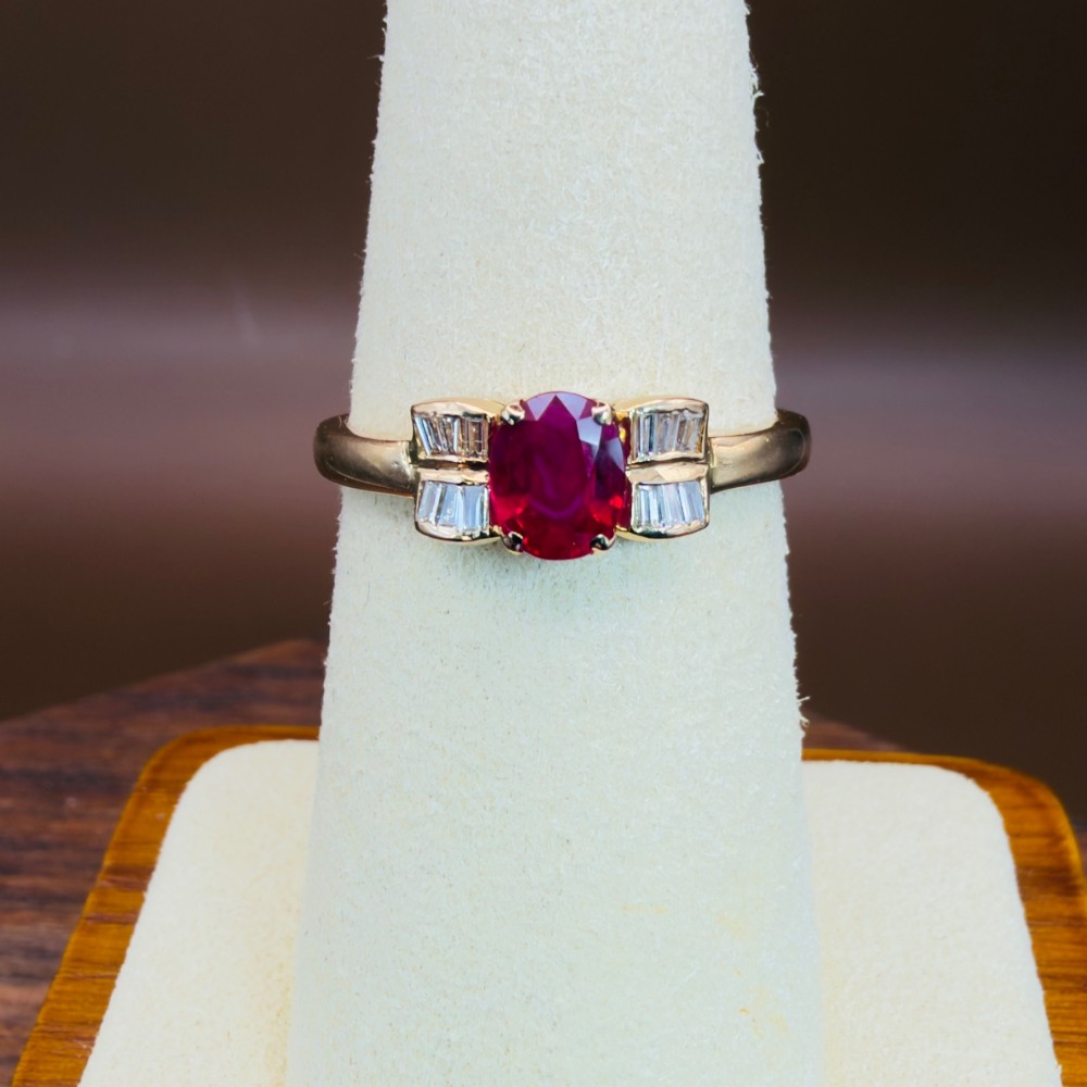 An 18ct yellow gold ring featuring an oval cut central red ruby flanked by stepped baguette cut diamonds on a polished band. View VI