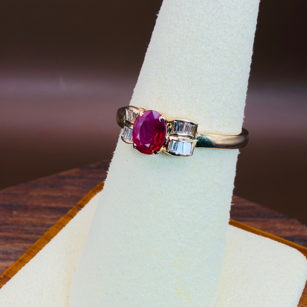 An 18ct yellow gold ring featuring an oval cut central red ruby flanked by stepped baguette cut diamonds on a polished band. View VII