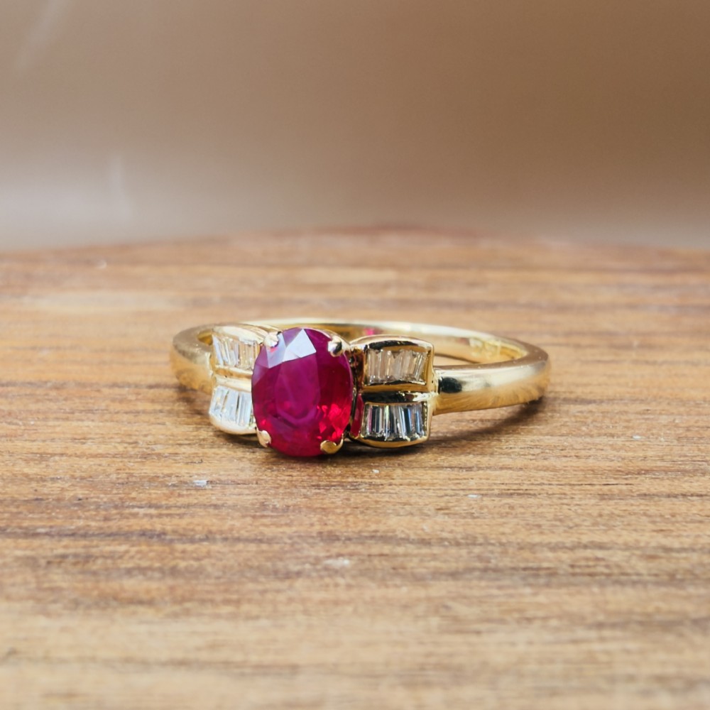 An 18ct yellow gold ring featuring an oval cut central red ruby flanked by stepped baguette cut diamonds on a polished band. View IX
