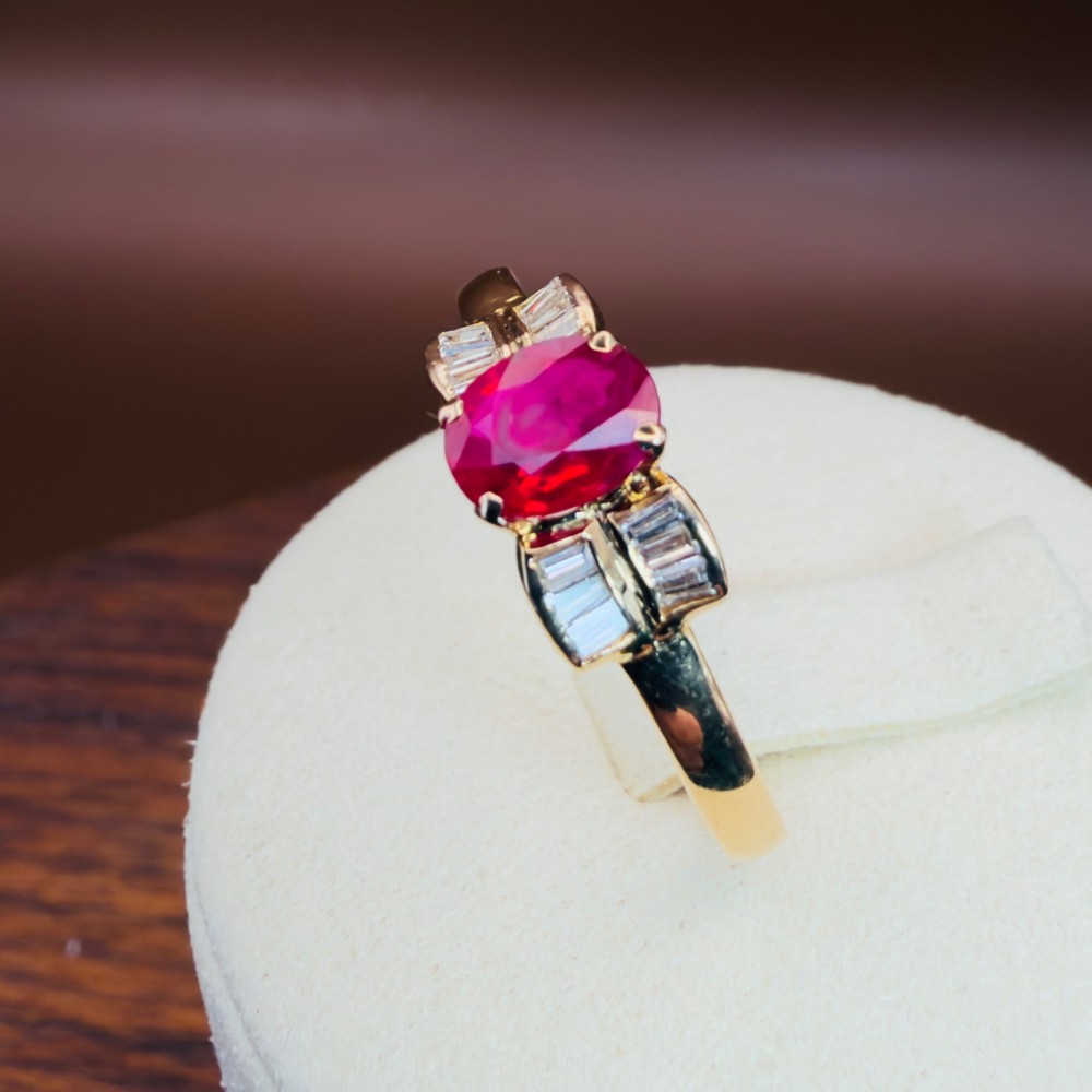 An 18ct yellow gold ring featuring an oval cut central red ruby flanked by stepped baguette cut diamonds on a polished band. View XI