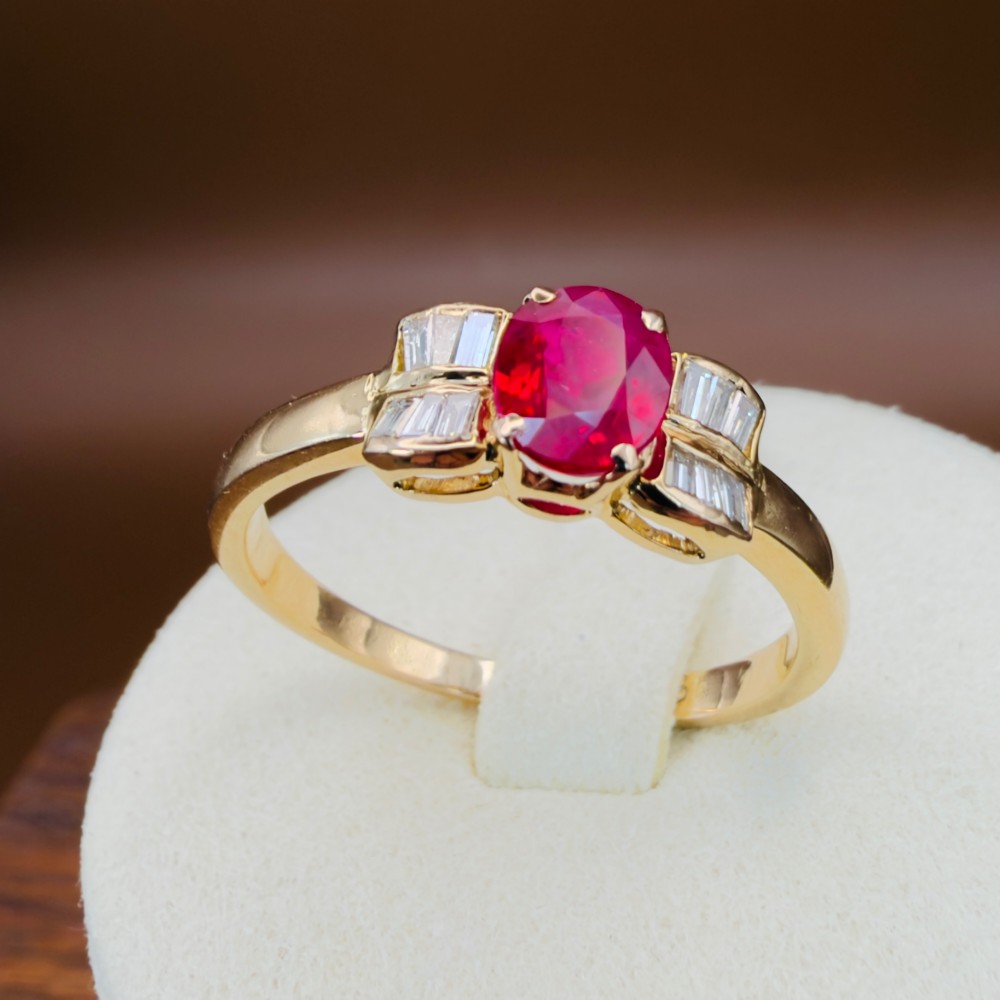 An 18ct yellow gold ring featuring an oval cut central red ruby flanked by stepped baguette cut diamonds on a polished band. View XII