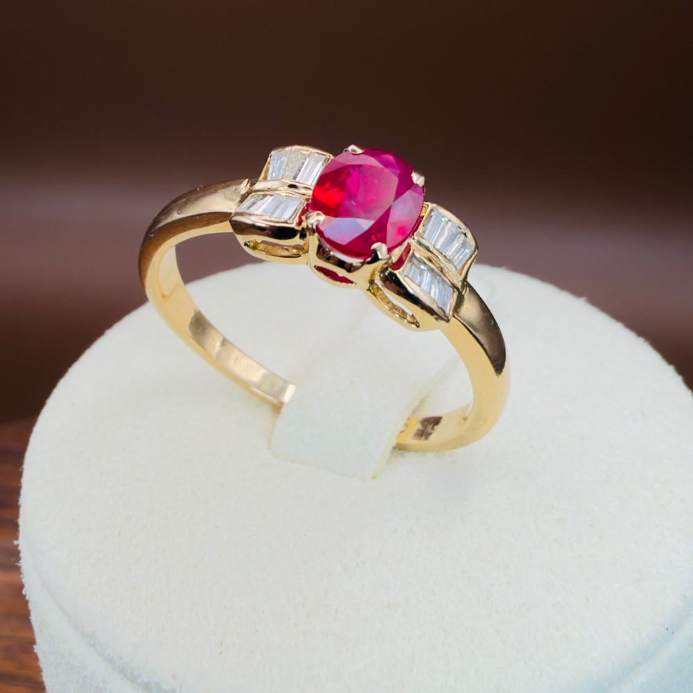 An 18ct yellow gold ring featuring an oval cut central red ruby flanked by stepped baguette cut diamonds on a polished band. View XIII