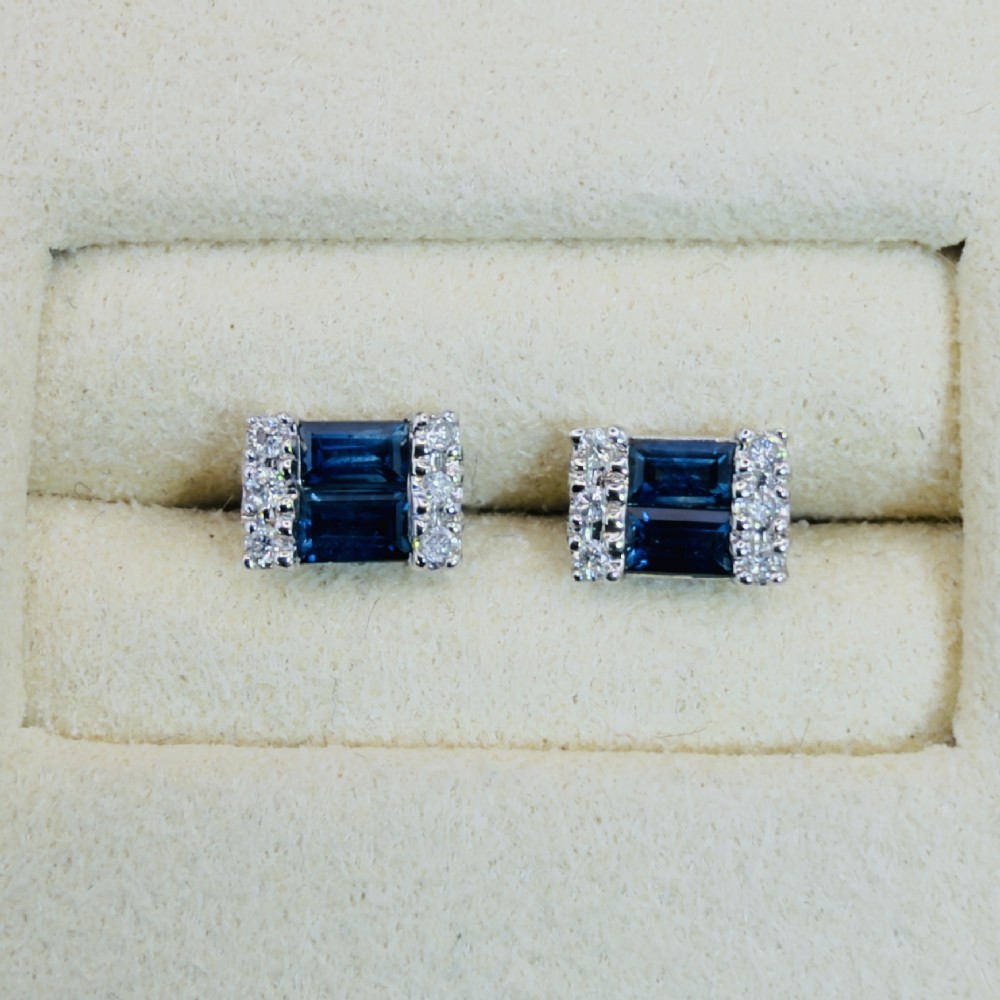 A pair of 9ct white gold stud earrings featuring two central emerald-cut blue sapphires flanked by small round diamonds.