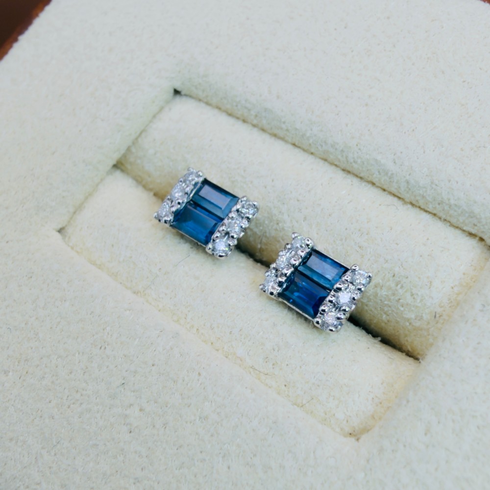 A pair of 9ct white gold stud earrings featuring two central emerald-cut blue sapphires flanked by small round diamonds. View II