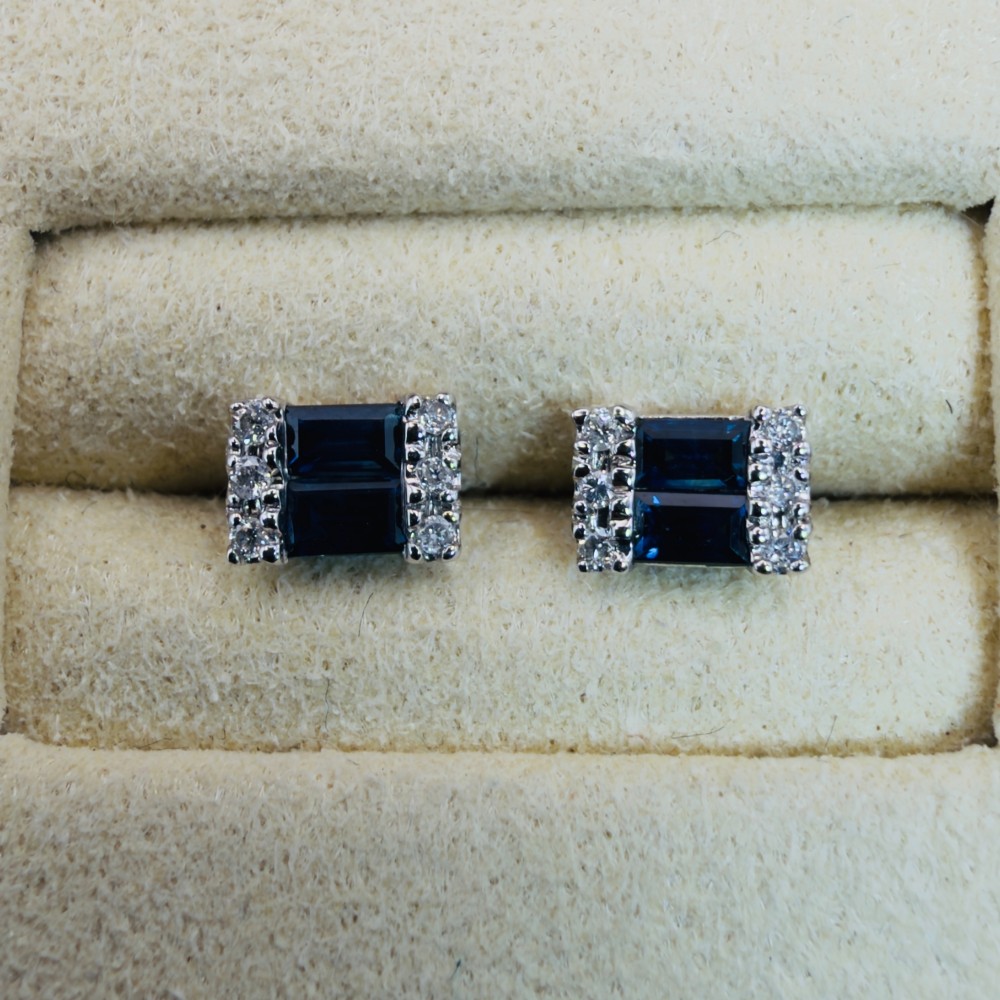 A pair of 9ct white gold stud earrings featuring two central emerald-cut blue sapphires flanked by small round diamonds. View IV