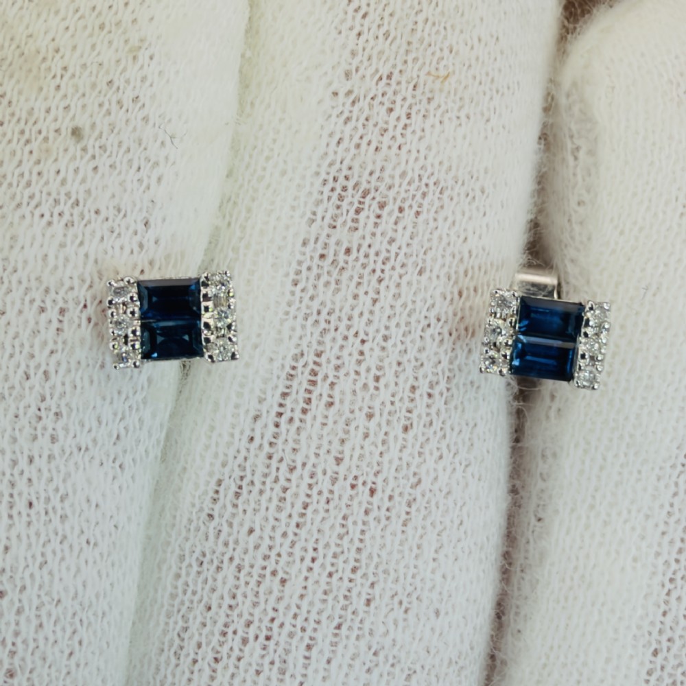 A pair of 9ct white gold stud earrings featuring two central emerald-cut blue sapphires flanked by small round diamonds. View VI