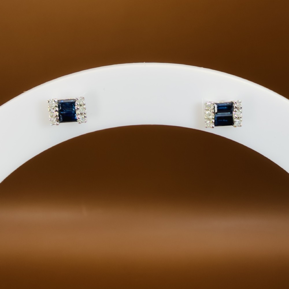 A pair of 9ct white gold stud earrings featuring two central emerald-cut blue sapphires flanked by small round diamonds. View IX