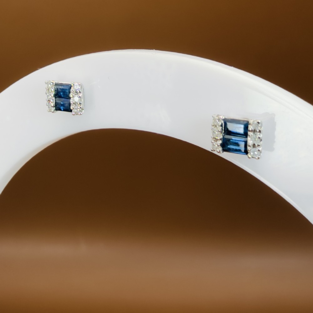 A pair of 9ct white gold stud earrings featuring two central emerald-cut blue sapphires flanked by small round diamonds. View X