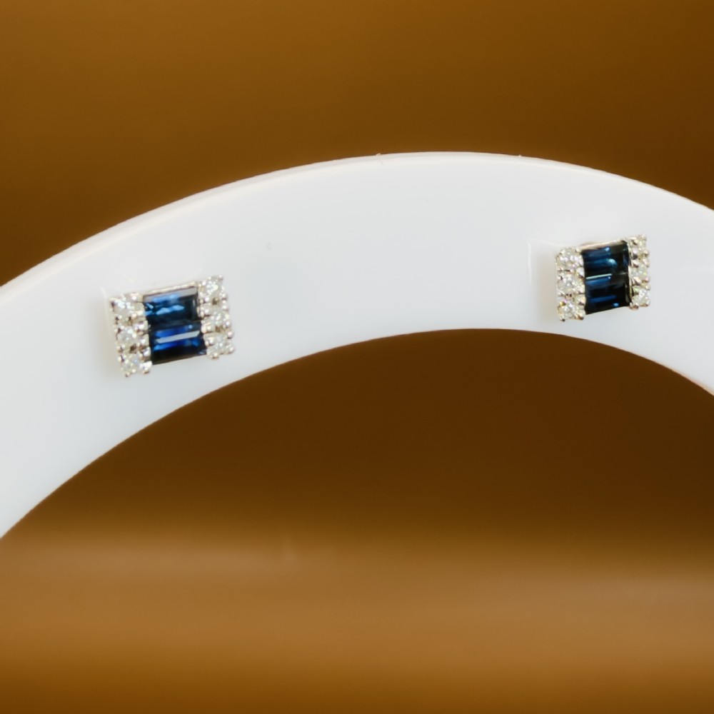 A pair of 9ct white gold stud earrings featuring two central emerald-cut blue sapphires flanked by small round diamonds. View XI