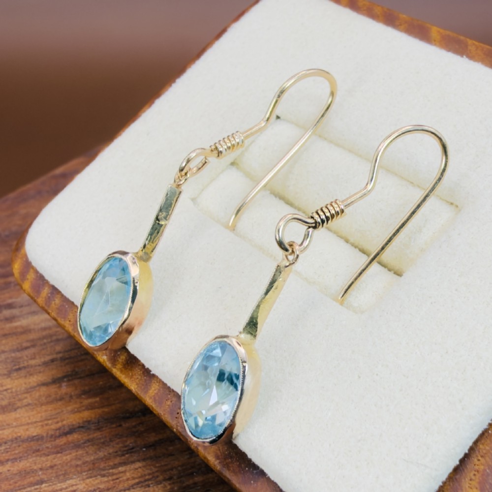 A pair of 9ct yellow gold Art Deco drop earrings featuring oval-cut light blue zircons suspended from vertical gold bars and shepherd hook wires. View III