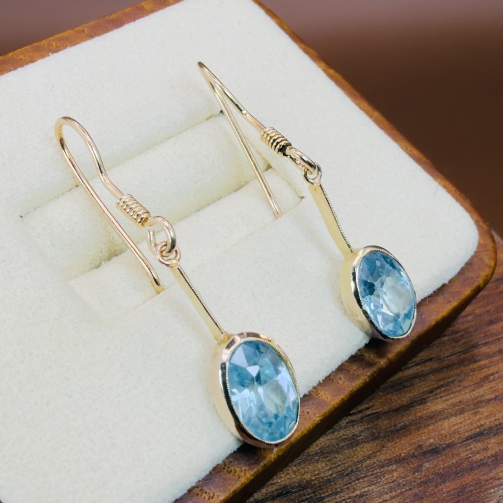 A pair of 9ct yellow gold Art Deco drop earrings featuring oval-cut light blue zircons suspended from vertical gold bars and shepherd hook wires. View II