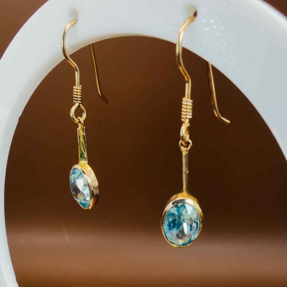 A pair of 9ct yellow gold Art Deco drop earrings featuring oval-cut light blue zircons suspended from vertical gold bars and shepherd hook wires. View VI