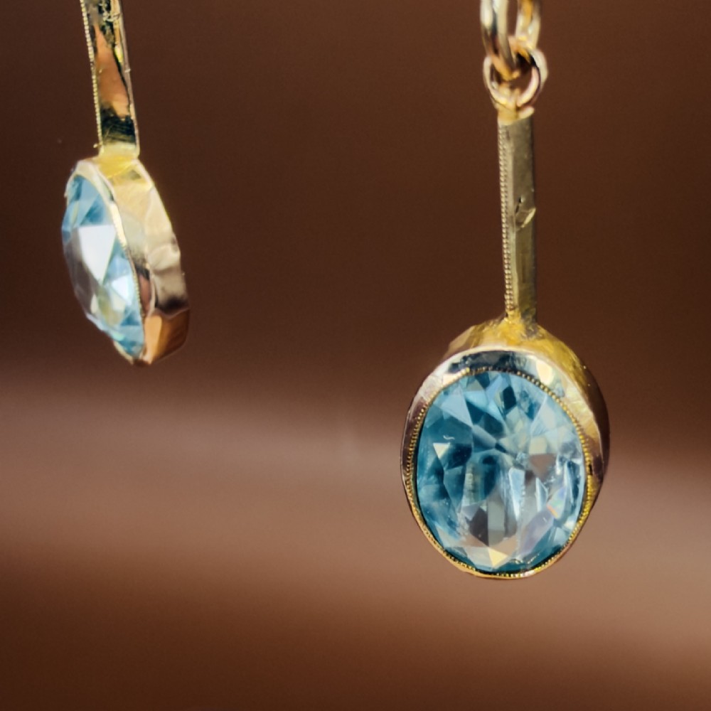 A pair of 9ct yellow gold Art Deco drop earrings featuring oval-cut light blue zircons suspended from vertical gold bars and shepherd hook wires. View IX