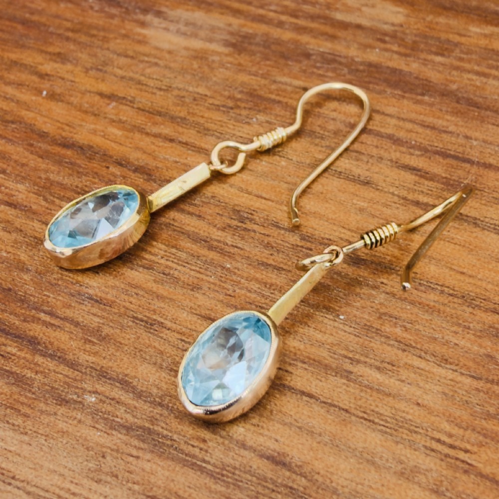 A pair of 9ct yellow gold Art Deco drop earrings featuring oval-cut light blue zircons suspended from vertical gold bars and shepherd hook wires. View XI