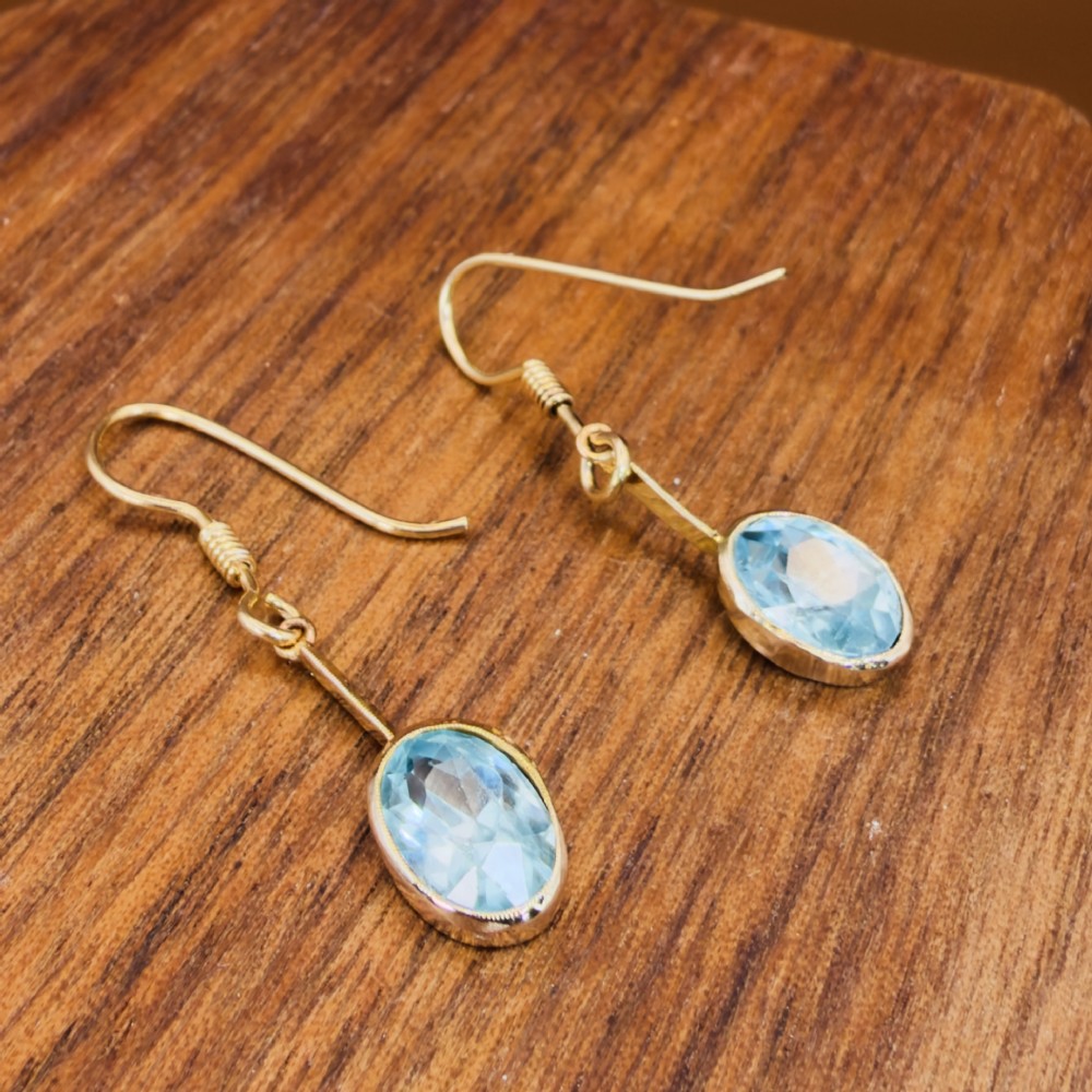 A pair of 9ct yellow gold Art Deco drop earrings featuring oval-cut light blue zircons suspended from vertical gold bars and shepherd hook wires. View XII
