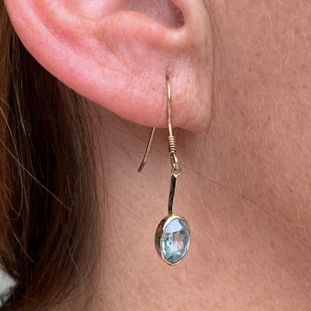 A pair of 9ct yellow gold Art Deco drop earrings featuring oval-cut light blue zircons suspended from vertical gold bars and shepherd hook wires. View XIII