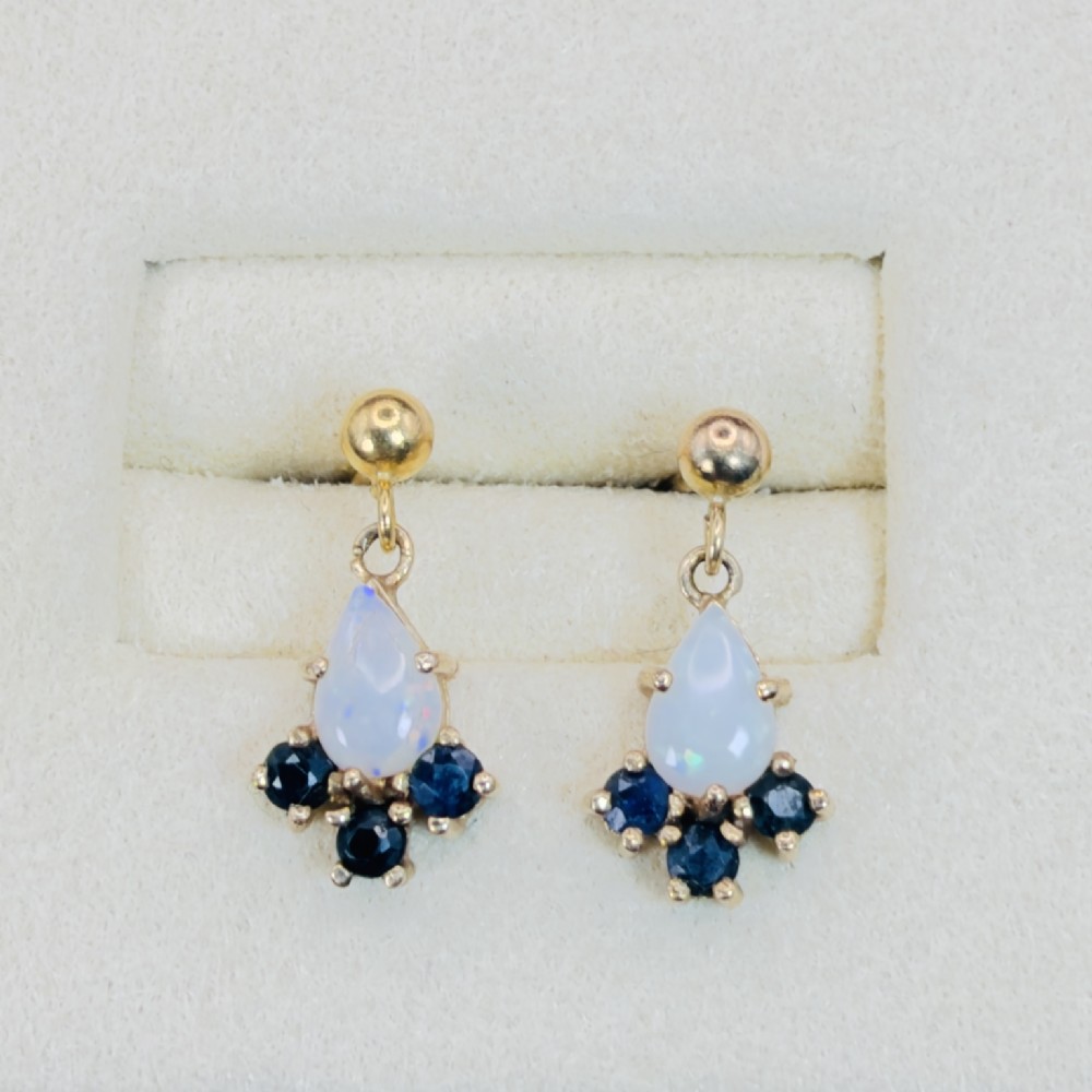A pair of 9ct yellow gold stud drop earrings featuring pear-shaped white opal cabochons accented with three round blue sapphires at the base. View II