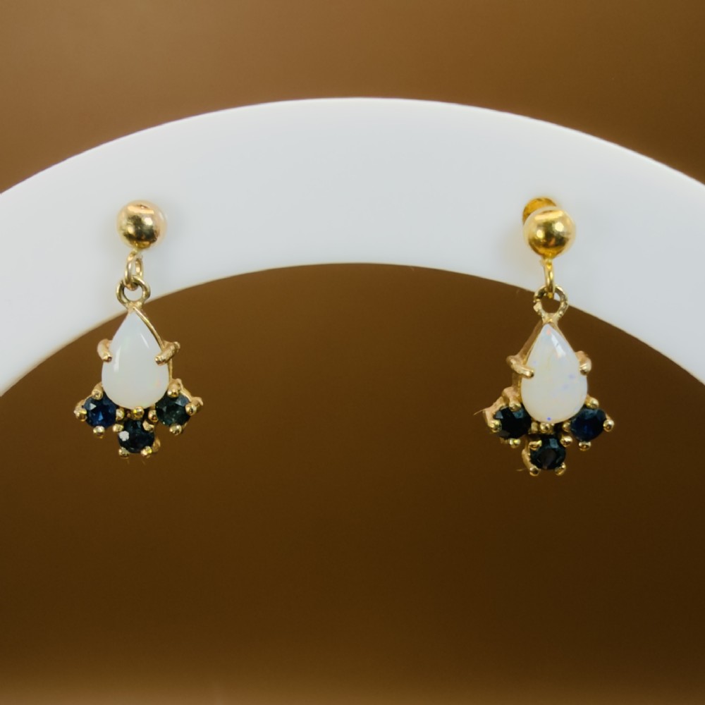 A pair of 9ct yellow gold stud drop earrings featuring pear-shaped white opal cabochons accented with three round blue sapphires at the base. View V