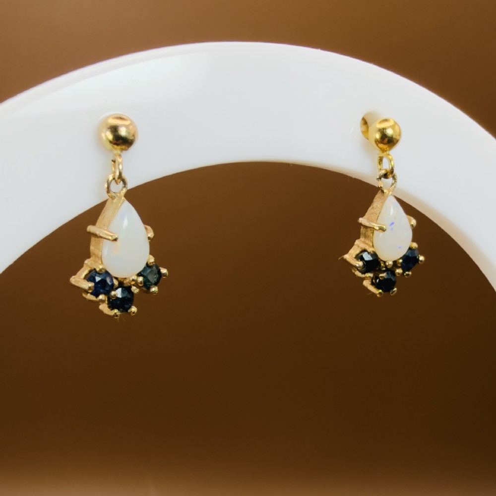 A pair of 9ct yellow gold stud drop earrings featuring pear-shaped white opal cabochons accented with three round blue sapphires at the base. View VII