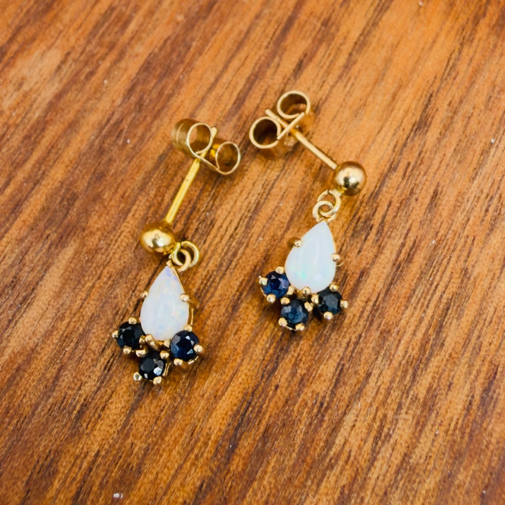 A pair of 9ct yellow gold stud drop earrings featuring pear-shaped white opal cabochons accented with three round blue sapphires at the base. View VIII