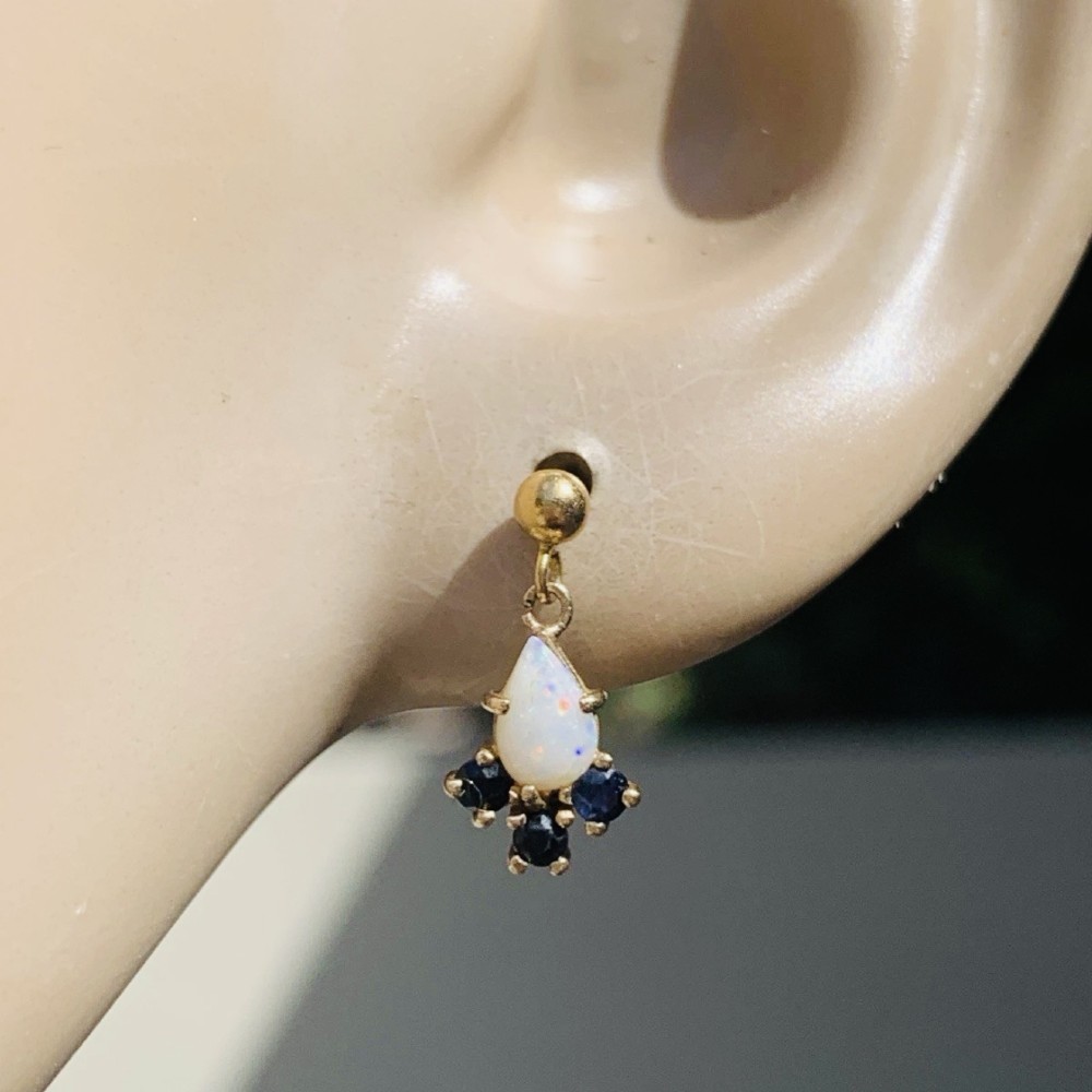 A pair of 9ct yellow gold stud drop earrings featuring pear-shaped white opal cabochons accented with three round blue sapphires at the base. View XI