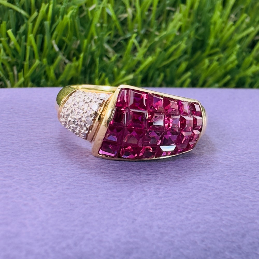 An 18ct yellow gold dress ring featuring a curved panel of princess cut red rubies alongside diamond set shoulders. View VIII