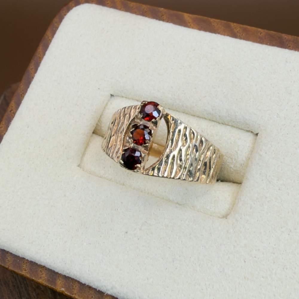 A 1960s 9ct yellow gold ring featuring a wide band with a bark effect texture and three vertically set round-cut deep red garnets. View III