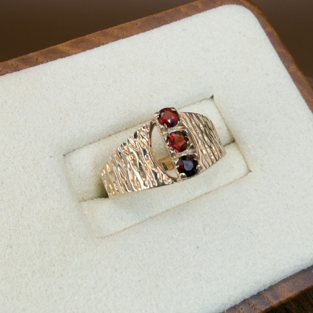 A 1960s 9ct yellow gold ring featuring a wide band with a bark effect texture and three vertically set round-cut deep red garnets. View IV
