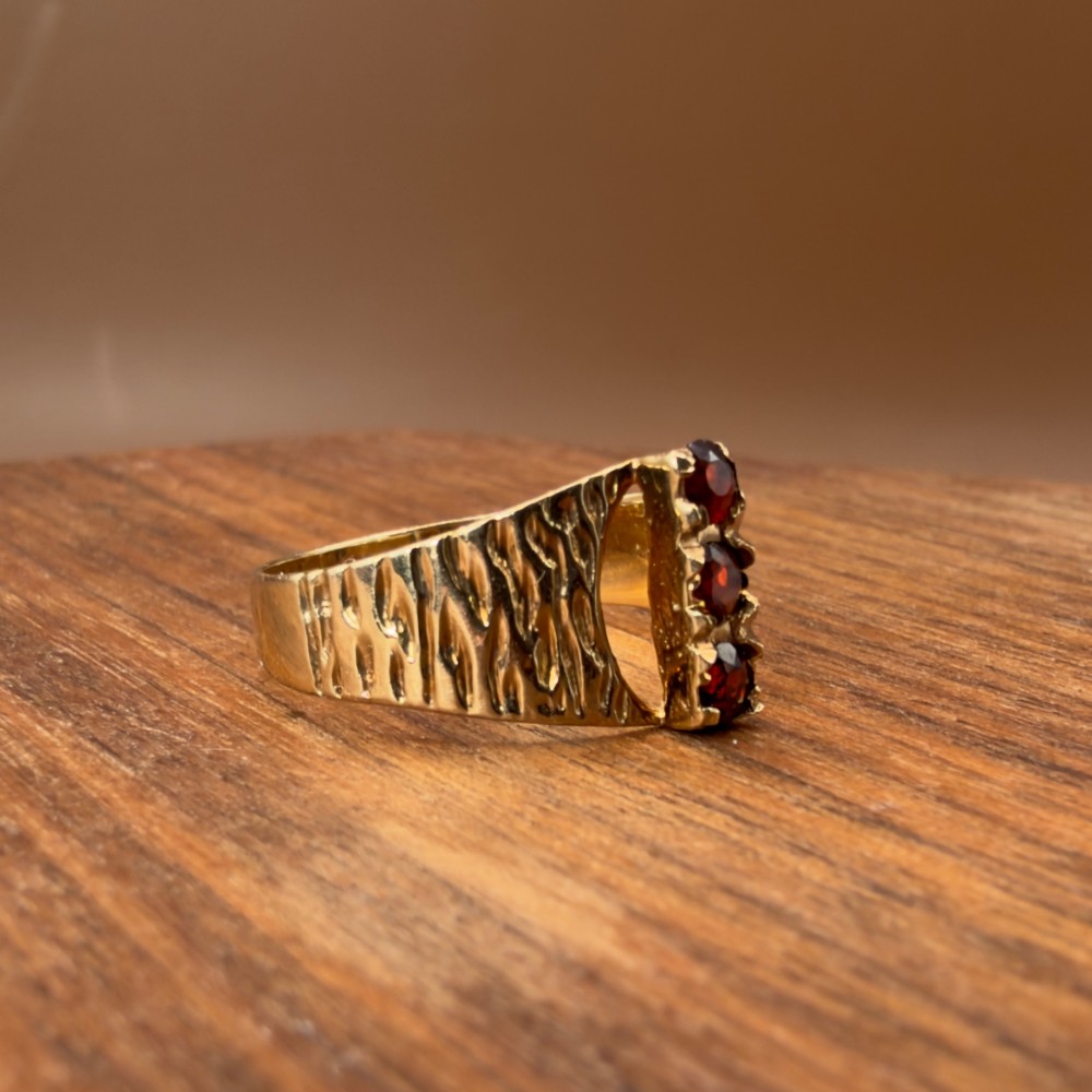 A 1960s 9ct yellow gold ring featuring a wide band with a bark effect texture and three vertically set round-cut deep red garnets. View VII