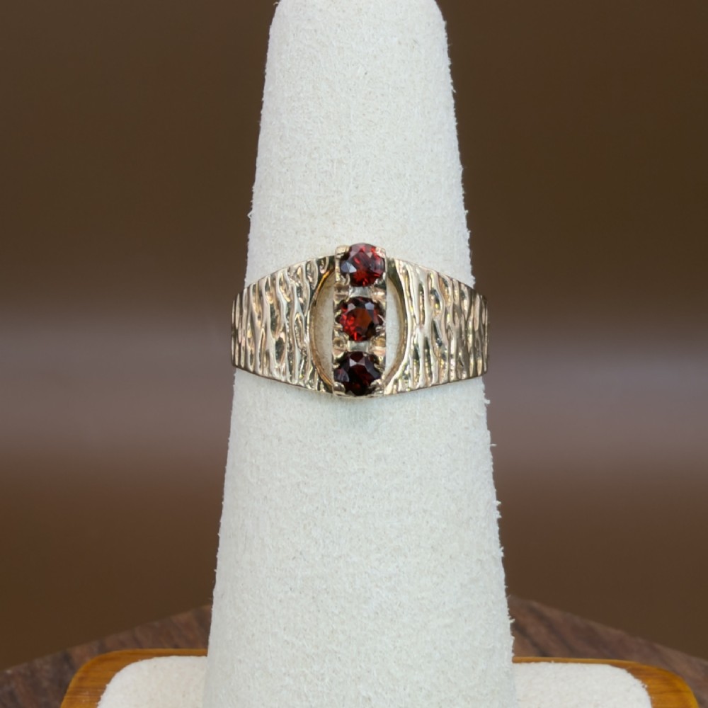 A 1960s 9ct yellow gold ring featuring a wide band with a bark effect texture and three vertically set round-cut deep red garnets. View VIII