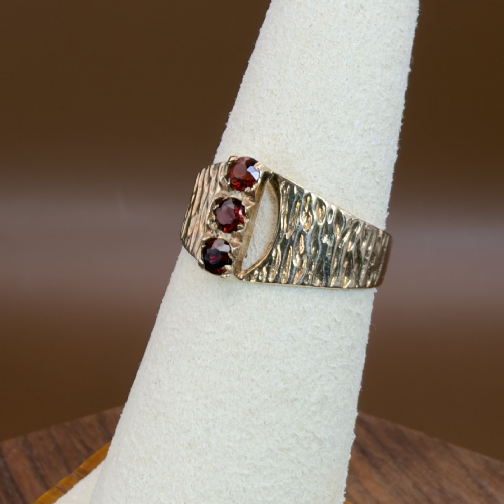 A 1960s 9ct yellow gold ring featuring a wide band with a bark effect texture and three vertically set round-cut deep red garnets. View IX