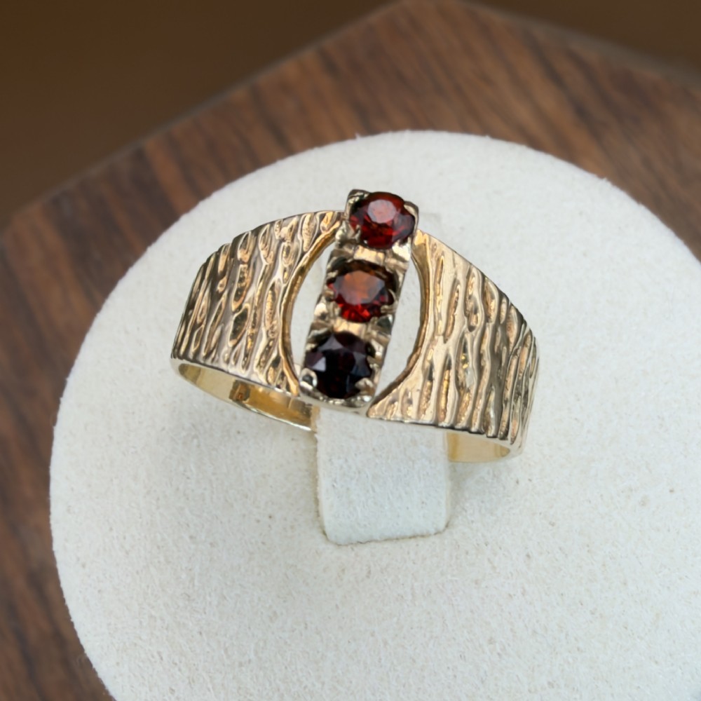 A 1960s 9ct yellow gold ring featuring a wide band with a bark effect texture and three vertically set round-cut deep red garnets.