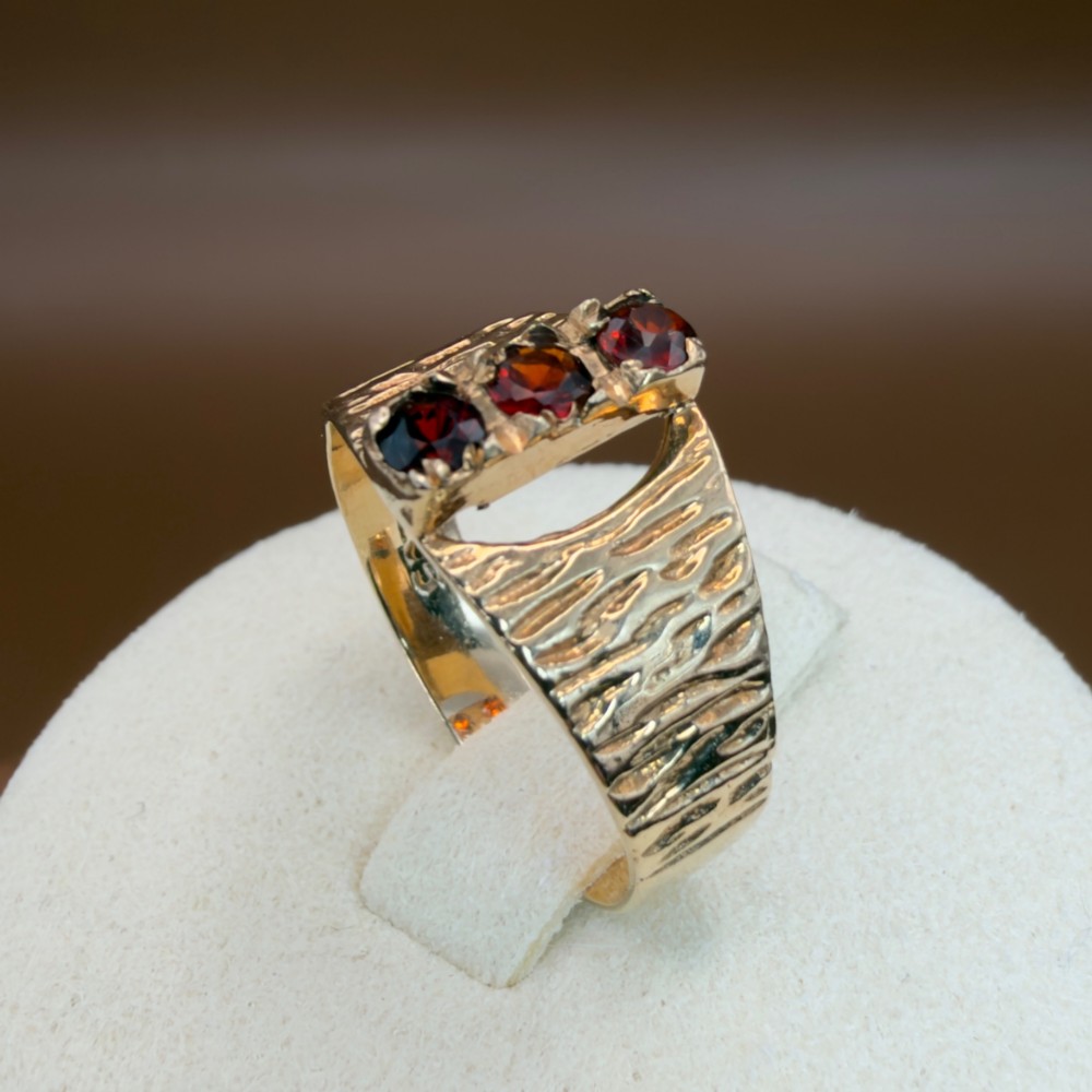 A 1960s 9ct yellow gold ring featuring a wide band with a bark effect texture and three vertically set round-cut deep red garnets. View XI