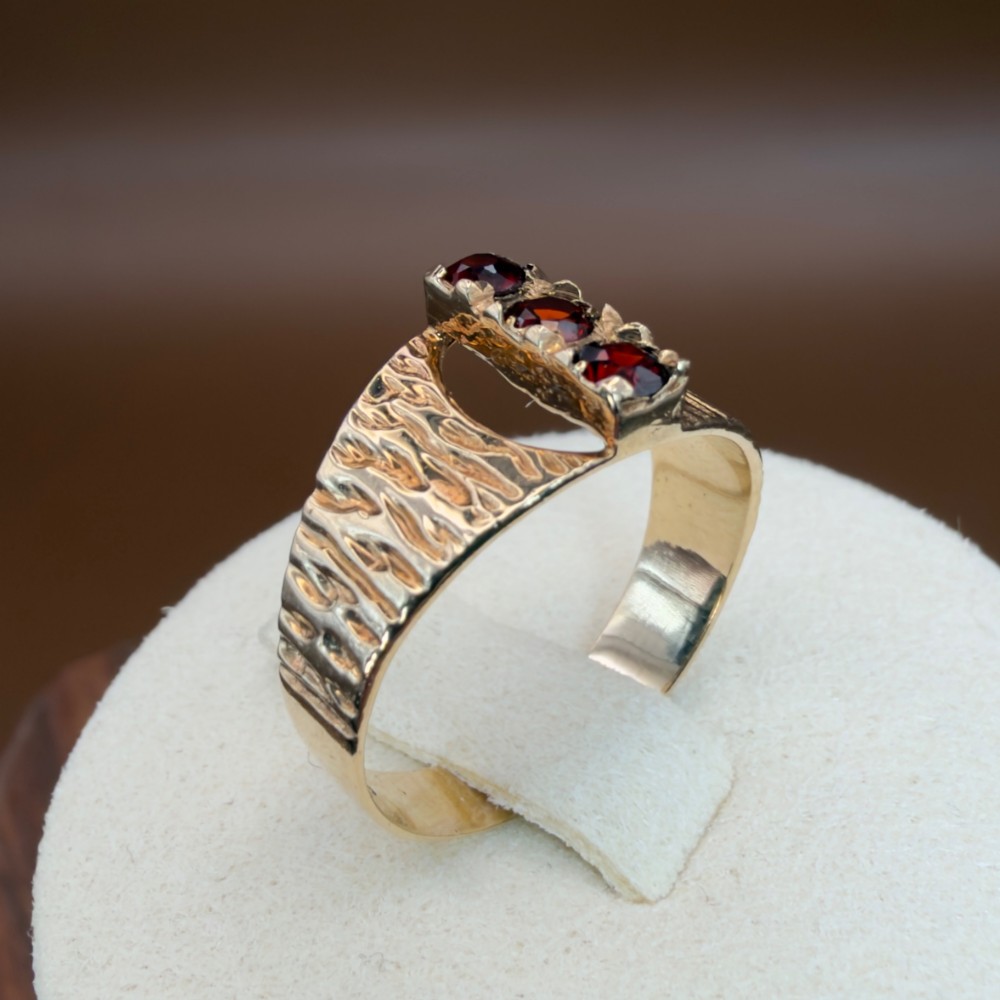 A 1960s 9ct yellow gold ring featuring a wide band with a bark effect texture and three vertically set round-cut deep red garnets. View XII
