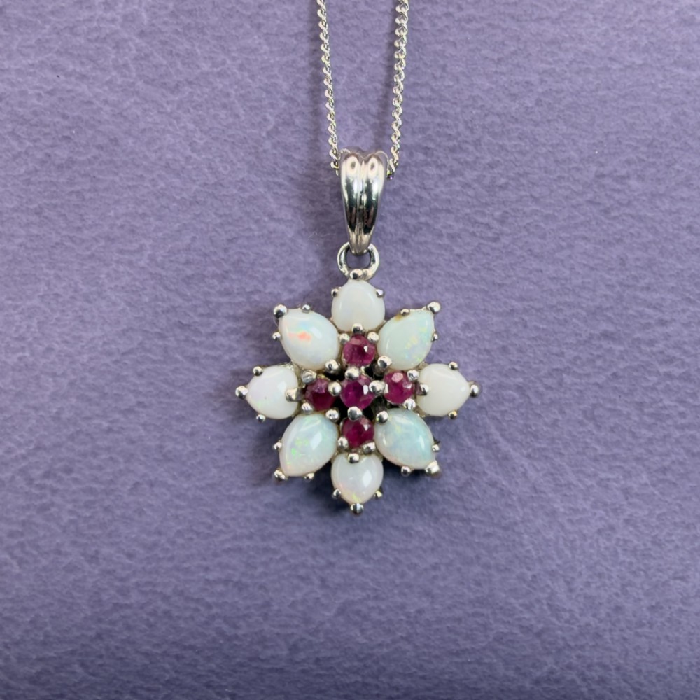 A 9ct white gold chain and cluster pendant featuring central red rubies surrounded by pear-shaped opals in a floral design.