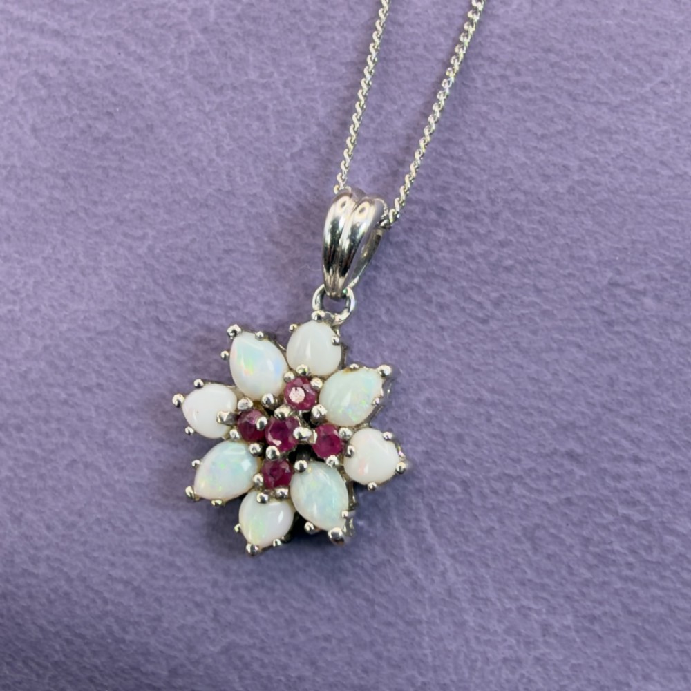 A 9ct white gold chain and cluster pendant featuring central red rubies surrounded by pear-shaped opals in a floral design. View II