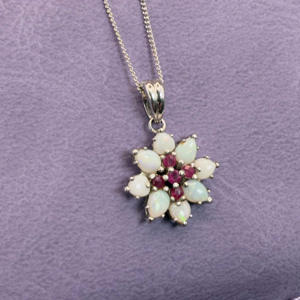 A 9ct white gold chain and cluster pendant featuring central red rubies surrounded by pear-shaped opals in a floral design. View III