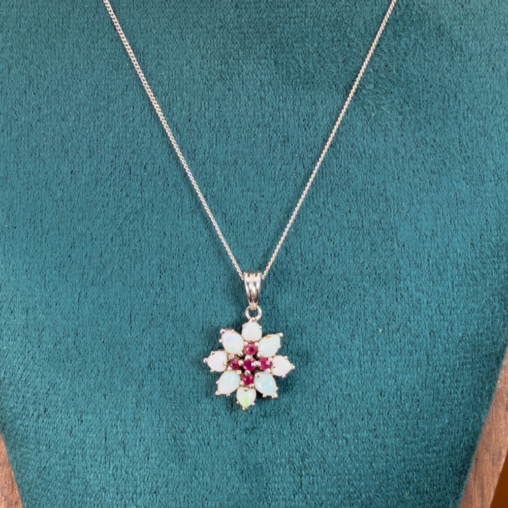 A 9ct white gold chain and cluster pendant featuring central red rubies surrounded by pear-shaped opals in a floral design. View IV