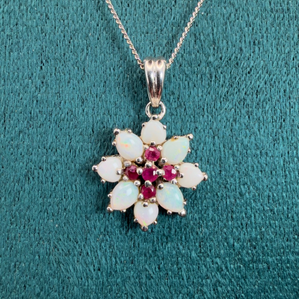 A 9ct white gold chain and cluster pendant featuring central red rubies surrounded by pear-shaped opals in a floral design. View V