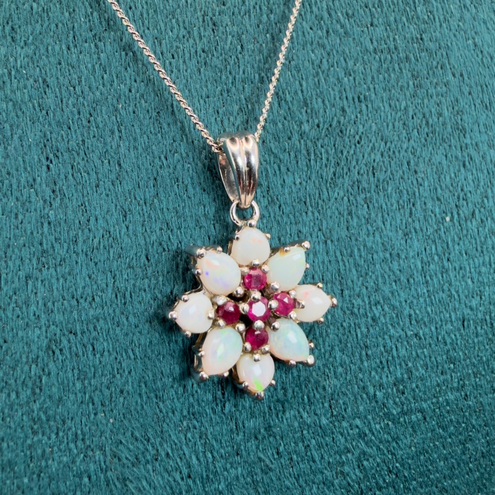 A 9ct white gold chain and cluster pendant featuring central red rubies surrounded by pear-shaped opals in a floral design. View VII