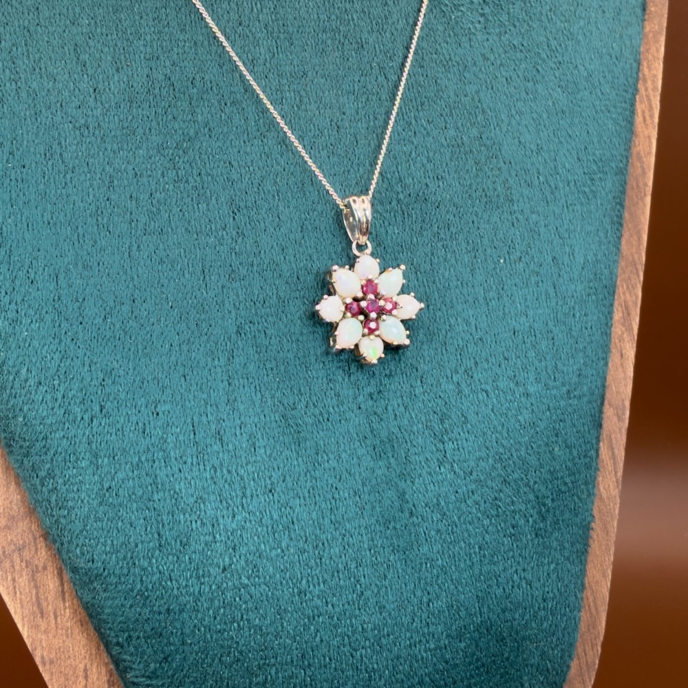 A 9ct white gold chain and cluster pendant featuring central red rubies surrounded by pear-shaped opals in a floral design. View VIII